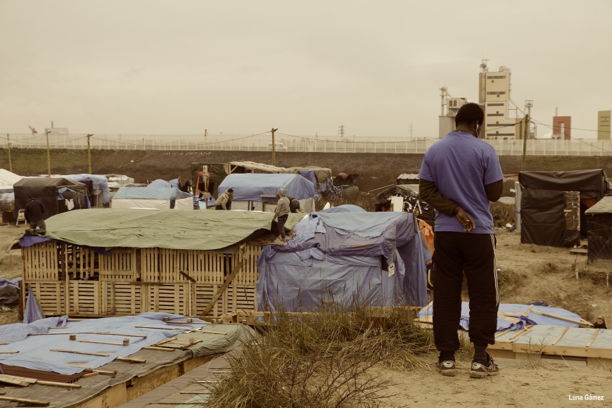 Un refugiado busca cobertura de móvil en una parte alta del campamento. Al fondo una valla separa el campamento de la carretera que lleva al puerto. / Foto: Luna Gámez