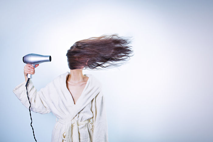 Una mujer se seca el pelo con secador de tal potencia que el pelo le cubre todo el rostro