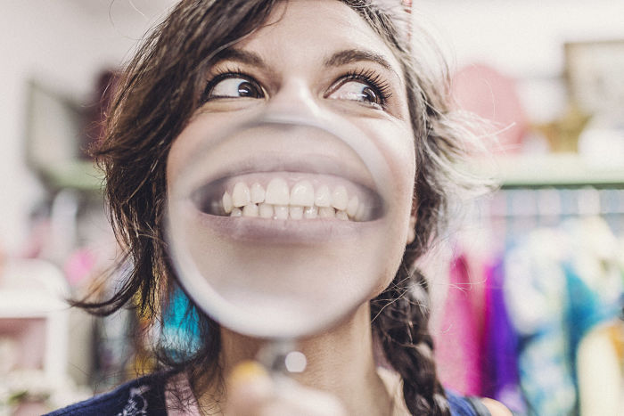 Rostro de una mujer cuya sonrisa aparece amplificada por una lupa pero que a la vez tiene mirada de sospecha