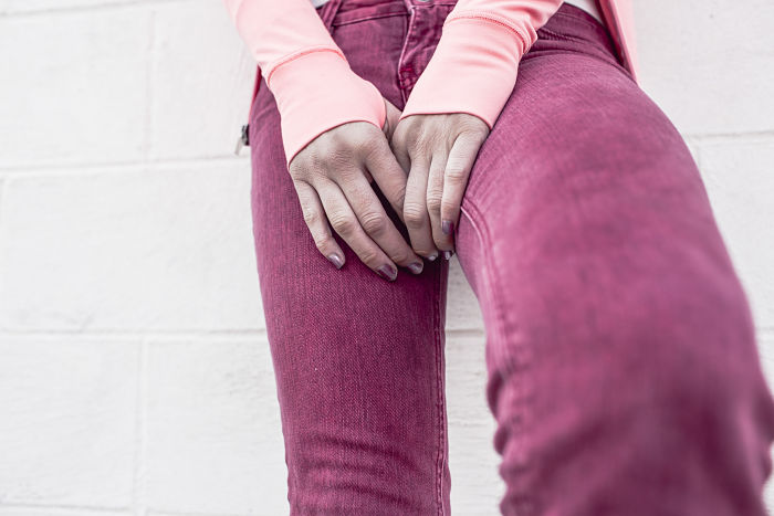 Una mujer forma un triángulo con sus manos, sobre su coxis, viste pantalones color fucsia