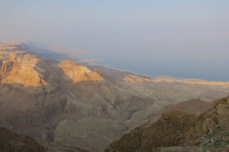 En la imagen se ve el mar desde una montaña rocosa marrón al atardecer.