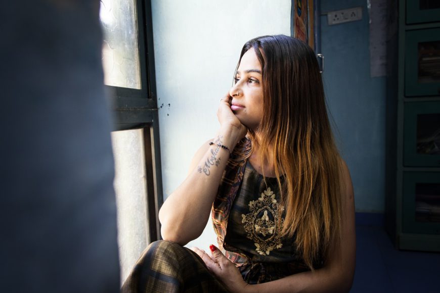 Una mujer con el pelo suelto posa de medio lado, mirando por una ventana