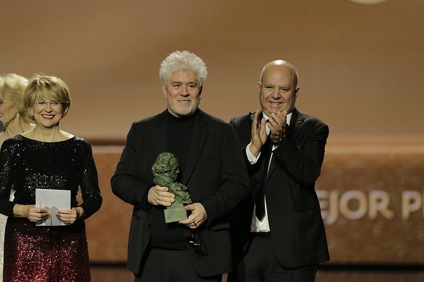 un hombre con el centro con el premio Goya, atrás uno hombre y una mujer