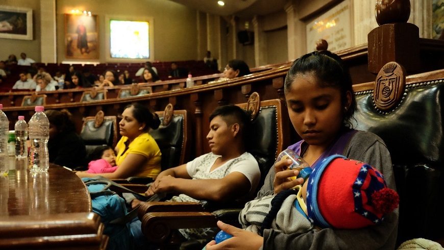 personas sentadas en la tribuna de un tribunal, en un primer plano una mujer da el biberón a un bebé