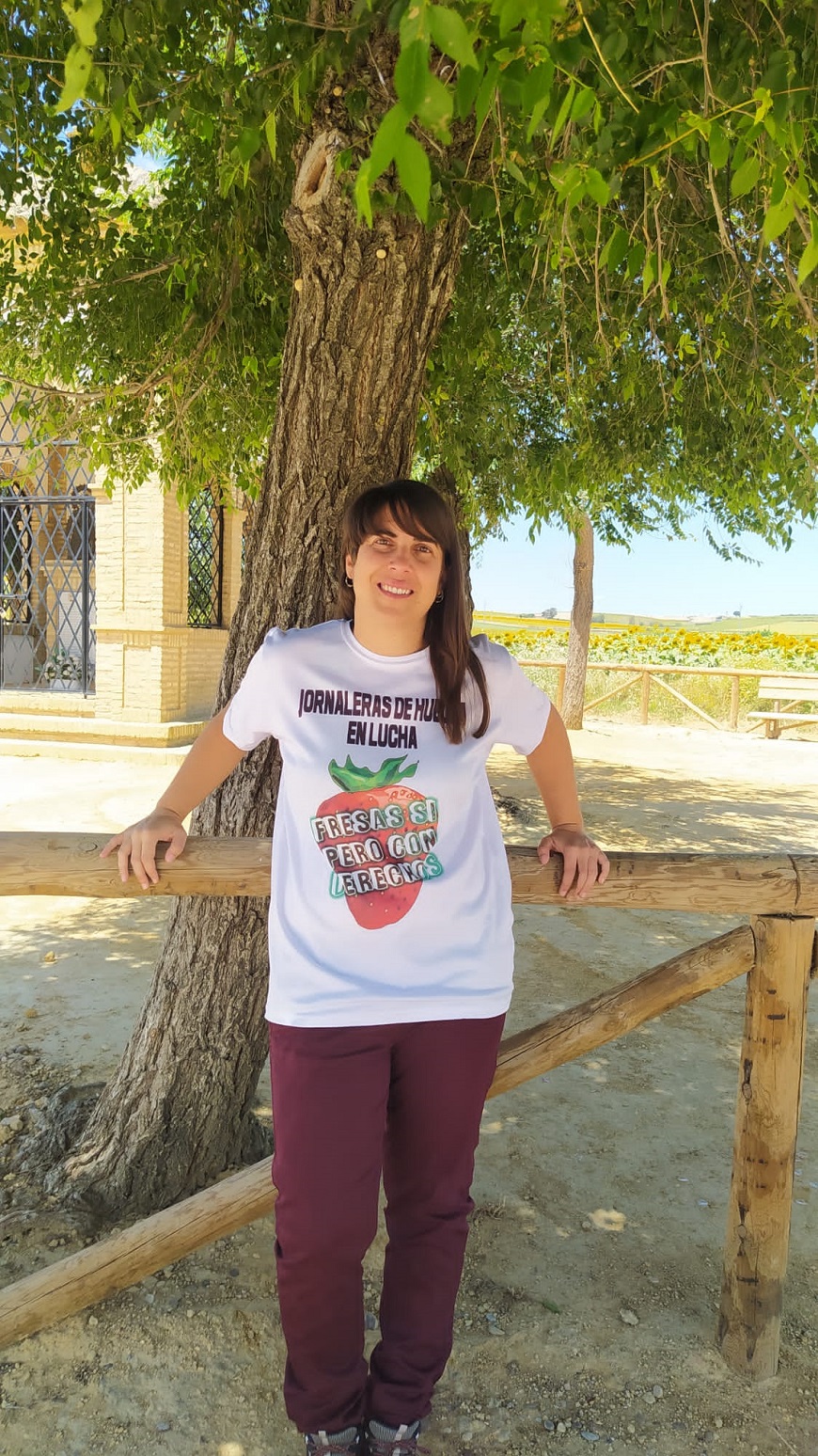 Una mujer posa apoyada en un árbol con una camiseta que denuncia la esclavitud en la recogida de la fresa. 