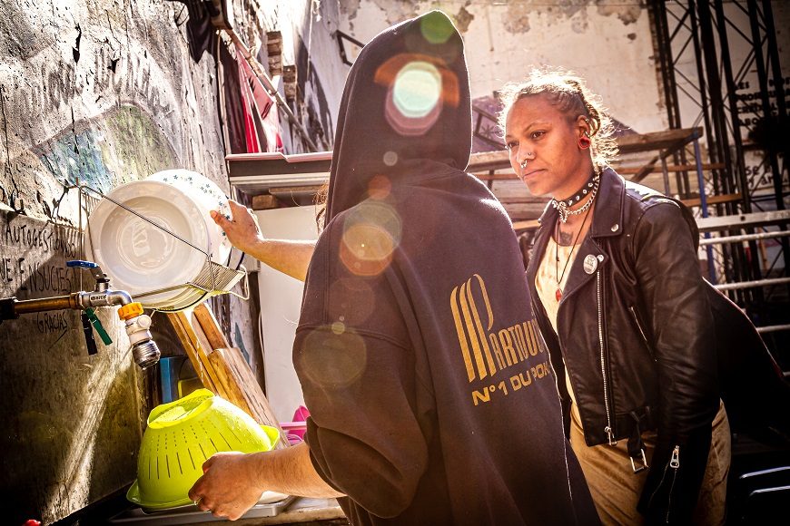 dos mujeres, bajo un sol radiante, lavan platos