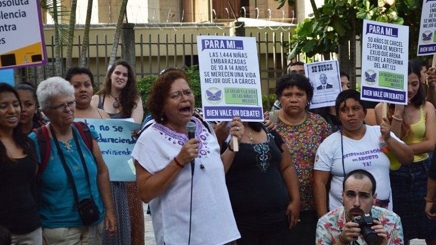 Un grupo de mujeres se manifesta con carteles. Una, en el centro, lleva un micrófono en la mano