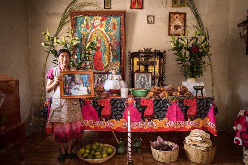 una mujer delante de su altar del Día de Muertos sostiene la foto de su madre