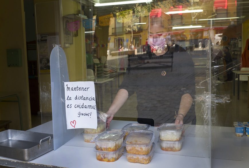 una mujer tras una mampara reparte comida