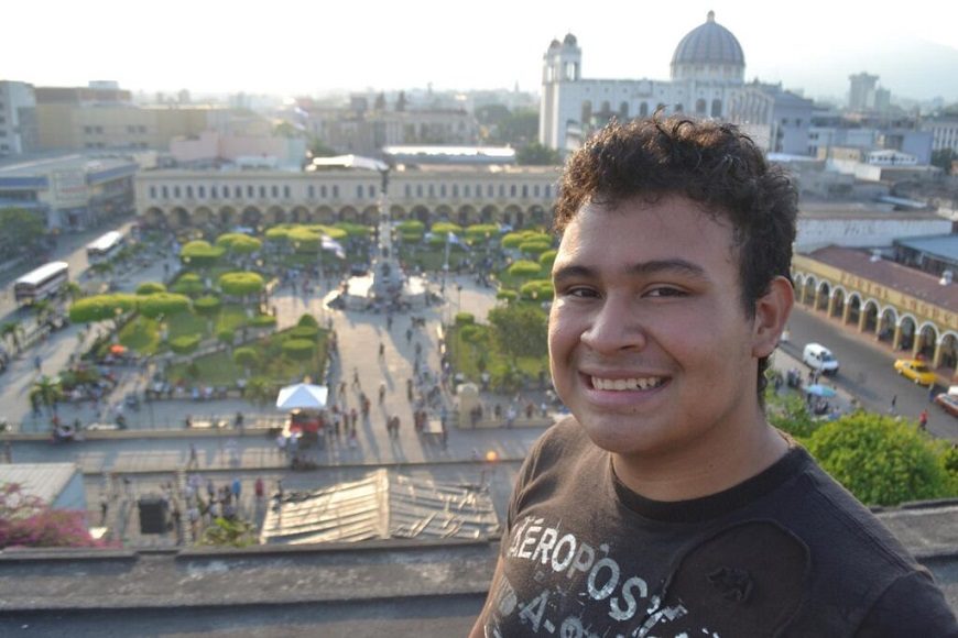 una persona posa, haciéndose un selfie, con el centro histórico de San Salvador de fondo