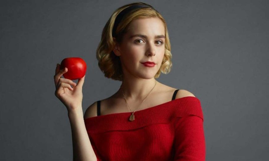 una chica de medio cuerpo vestida de rojo tiene una manzana roja en la mano