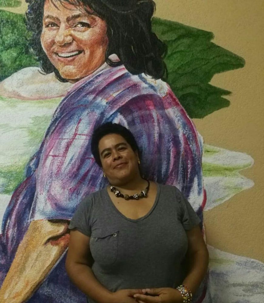 una mujer posa delante de un mural de Berta Cáceres