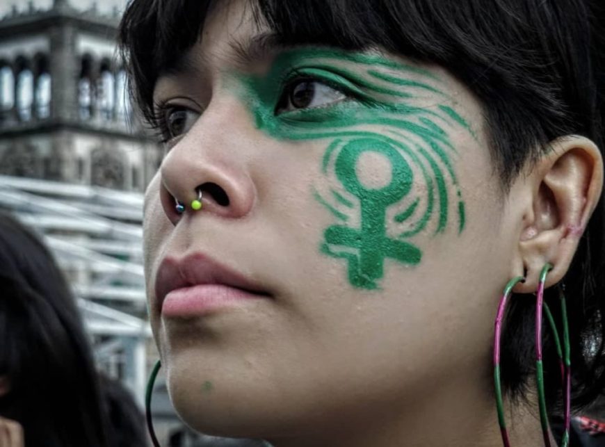 primer plano de una mujer en una manifestación, lleva la cara con pintadas verdes