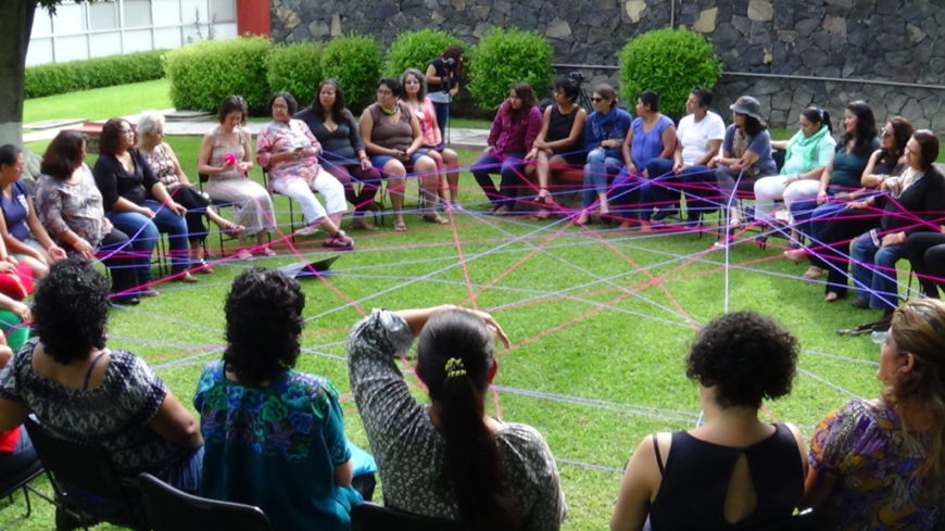 una mujeres sentadas en círculo en un jardín unidas por lana