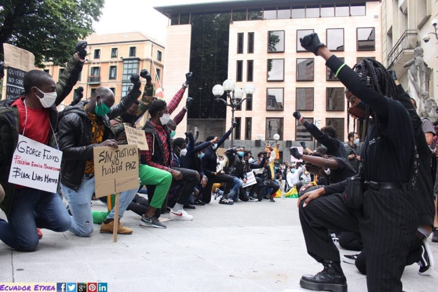 una grupo de manifestantes, personas negras, con rodilla al suelo y brazo en alto