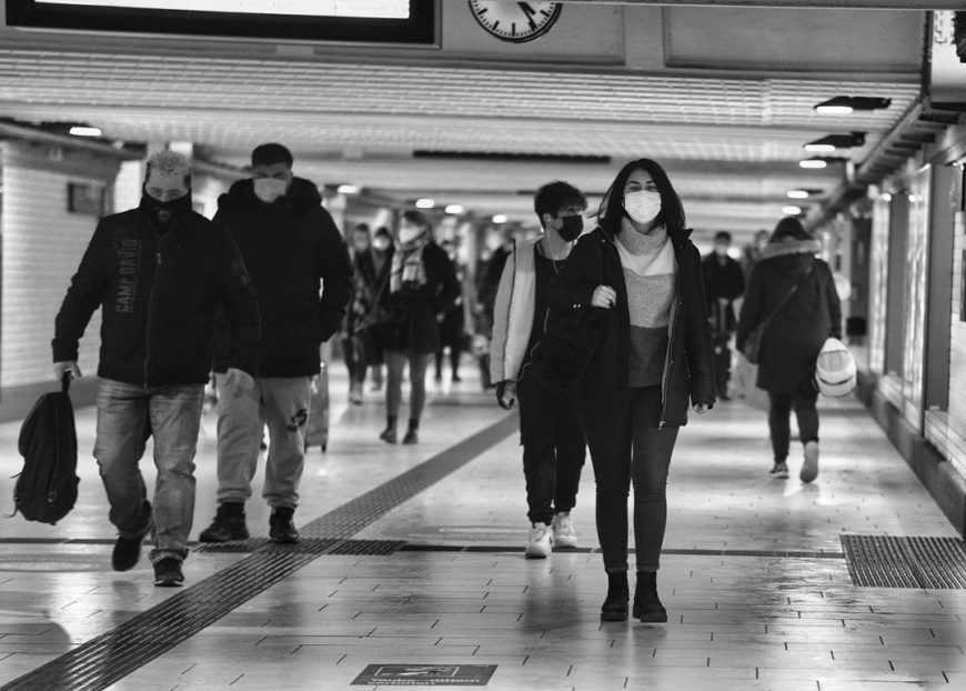 un grupo de personas camina con mascarilla. foto en blanco y negro, parace el interior de una estación de transporte