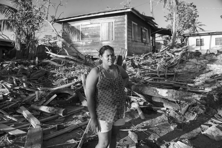 una mujer posa delante de los escombros de varias casas. foto en blanco y negro