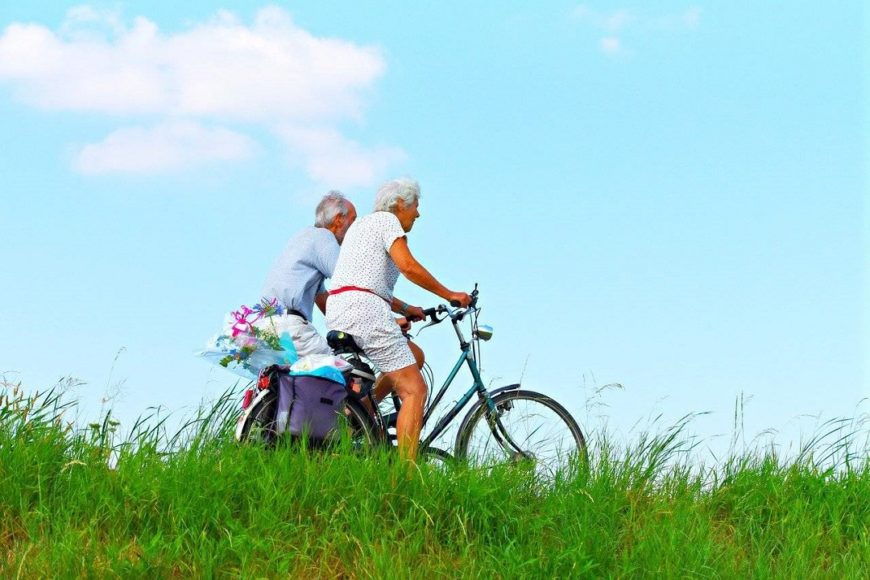 un hombre y una mujer mayor en bici, en un campo verde y con el cielo muy azul