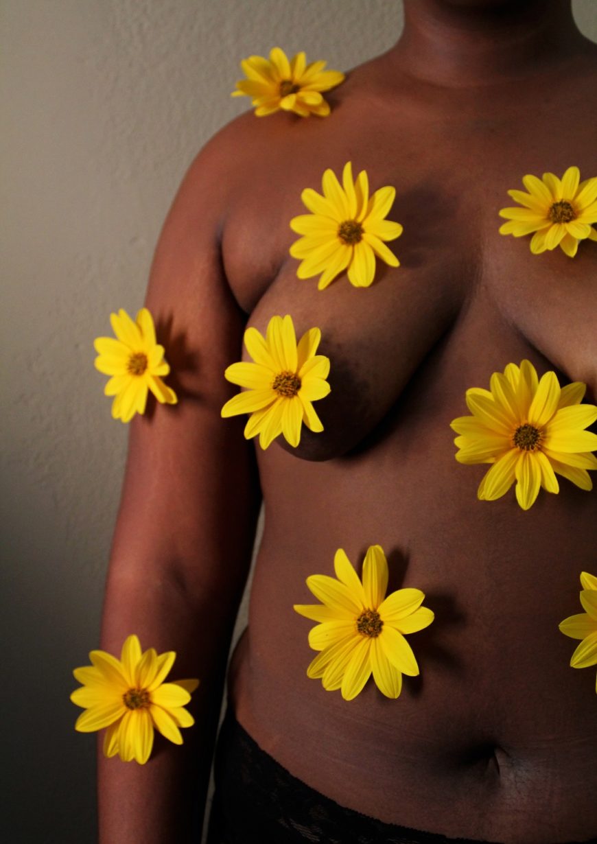 medio cuerpo con el torso desnudo de una mujer negra, que lleva puestas flores amarillas