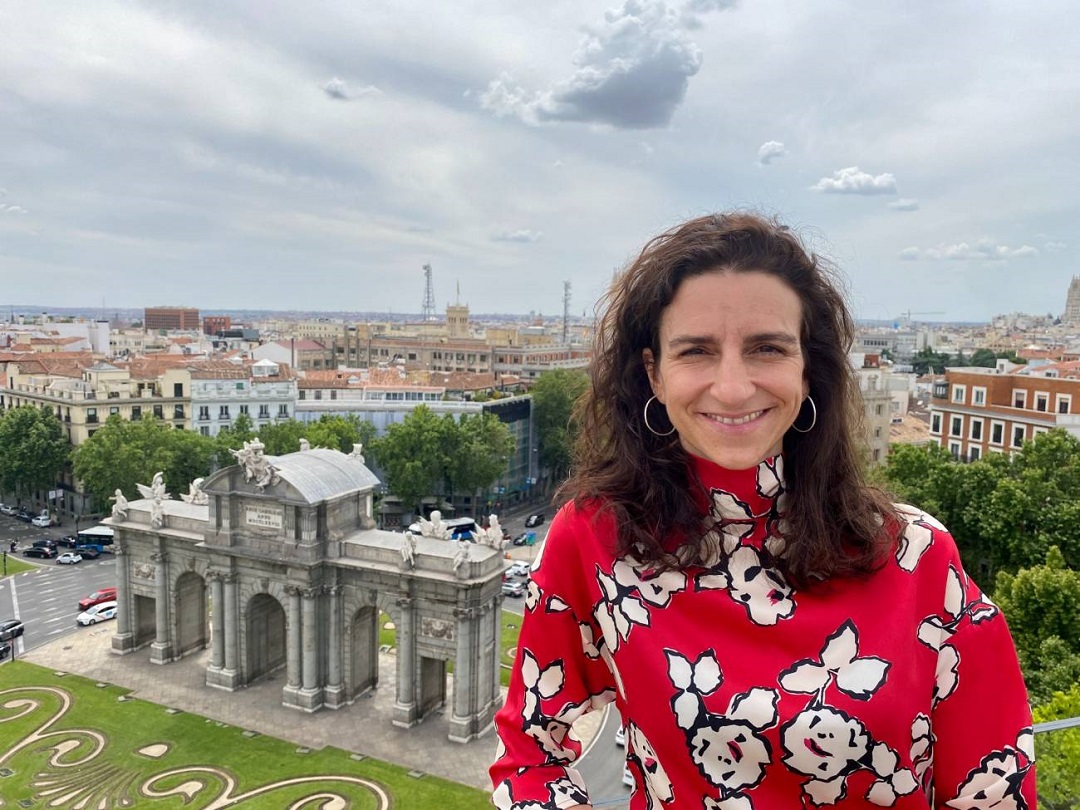 una mujer posa y se ve al fondo y abajo la Puerta de Alcalá de Madrid