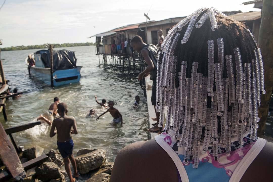 jóvenes negros juegan en el agua del mar en una zona con casas sobre el agua muy pobres