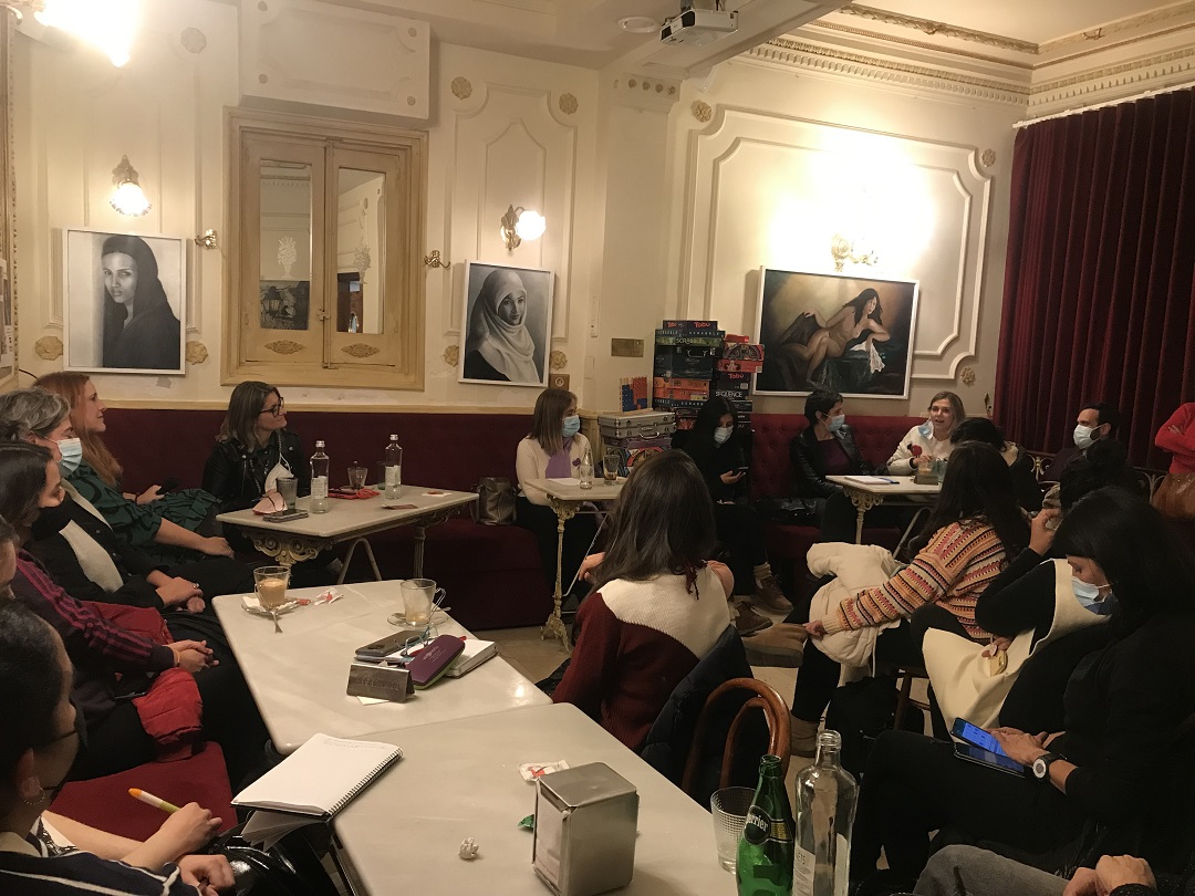 una sal de un bar con decoración clásica con varias mujeres sentadas en las mesas a modo de debate